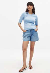 Šviesiai mėlynas trumpas megztinis su trumpomis rankovėmis derinamas su aukšto liemens džinsinėmis šortais. Megztinis turi apvalų iškirpimą ir prigludusią siluetą.