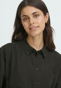 Dark green collared shirt made from a lightweight, soft fabric featuring a subtle texture, two chest pockets, and front button closure.