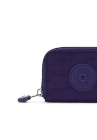 Portafoglio in tessuto viola con zip, dotato di patch circolare con logo Kipling e zip coordinata, su sfondo bianco.