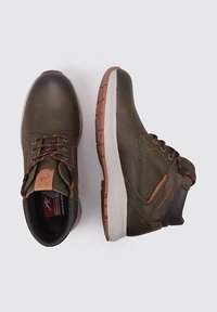 Botas de cuero verde oscuro con detalles en marrón, que presentan un diseño de cordones, puntera redonda, collar acolchado y una suela de goma con agarre texturizado.