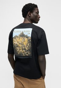 Μαύρο βαμβακερό t-shirt με μεγάλο, πολύχρωμο σχέδιο της κοιλάδας Yosemite και το κείμενο «ΦΥΤΑ & ΧΛΩΡΙΔΑ» τυπωμένο στην πλάτη.