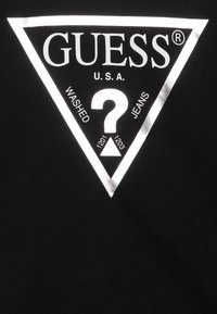T-shirt en coton noir avec un grand logo triangulaire blanc portant "GUESS U.S.A." et un point d'interrogation central, rehaussé de détails réfléchissants.