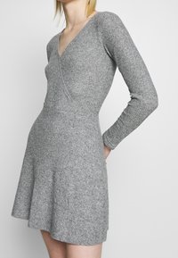 Robe grise à manches longues avec un décolleté en V, en maillon texturé, avec un corsage ajusté et une jupe évasée, présentant une finition lisse et des coutures discrètes.