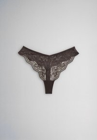 String en dentelle noire avec motifs floraux, bords festonnés et partie d’entrejambe en tissu uni, présenté à plat sur un fond gris clair.