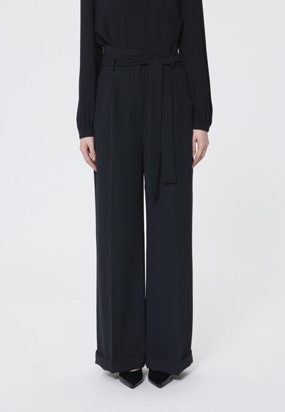 Pantaloni neri a gamba larga con vita alta, dotati di cintura e tasche laterali. Tessuto liscio e orli con polsini. Design minimalista.