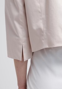 Lichtroze cropped jack met een gestructureerde afwerking, voorzien van zijsplitten en een ontspannen pasvorm, gedragen over een witte top.