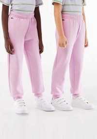 Pantalons de survêtement roses avec taille élastique et poignets, associés à des baskets blanches avec des straps Velcro. Texture légère, coupe décontractée, sans motifs.
