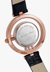 Reloj de acero inoxidable redondo con bisel de oro rosa y correa de cuero negra. Presenta un fondo de caja transparente que muestra el movimiento.