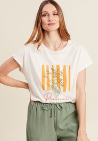 T-shirt blanc à manches courtes avec un design de ligne orange, un graphisme de vase vert avec des feuilles, et le texte "Provence" en rouge. Matériau doux.