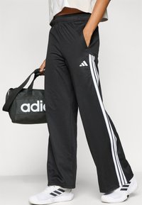 Črne atletske hlače z belimi črtami ob straneh, z elastičnim pasom in žepi. Kombinirane s črno torbo in belimi supergami.
