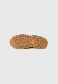 Sole av brun gummistøvlette for fotturer med dyp mønsterdesign og liten oransje sirkel logo i midten på hvit bakgrunn.