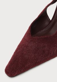 Gros plan d'une chaussure bordeaux à bout pointu avec une surface texturée et duveteuse et une ouverture basse, montrant la doublure intérieure en cuir.