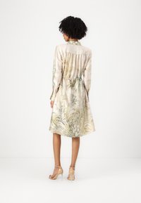 Abito in seta a maniche lunghe con stampa botanica in morbidi toni di verde e beige. Forma svasata con colletto abbottonato e dettagli di arricciatura sul retro.