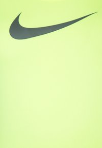 Neonowo żółta sportowa koszulka o gładkiej fakturze z dużym czarnym logo Nike swoosh na przodzie.