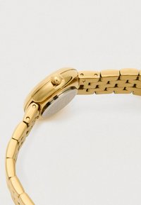 Złoty metalowy pasek do zegarka z złotą kopertą zegarka, widok z boku na białym tle.