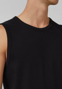 Schwarzes ärmelloses, geripptes Tanktop mit Rundhalsausschnitt. Verfügt über eine glatte Textur und subtile Nähdetails entlang der Kanten.