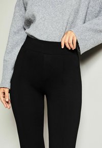Leggings noirs taille haute avec une texture lisse, associés à un pull oversize gris clair avec des poignets côtelés.