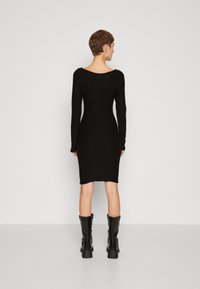 Black long-sleeve bodycon dress with a scoop neck, made from a smooth fabric, and ending just above the knee. Paired with knee-high black boots.
