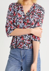Blusa floreale in tessuto azzurro chiaro con motivo floreale rosso e verde. Presenta un collo a V, maniche a tre quarti e una vestibilità morbida.