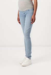 Vaqueros skinnies de denim azul claro con un diseño estándar de cinco bolsillos, ajuste de cintura media y un ligero desgaste en los muslos. Combinados con zapatillas blancas.