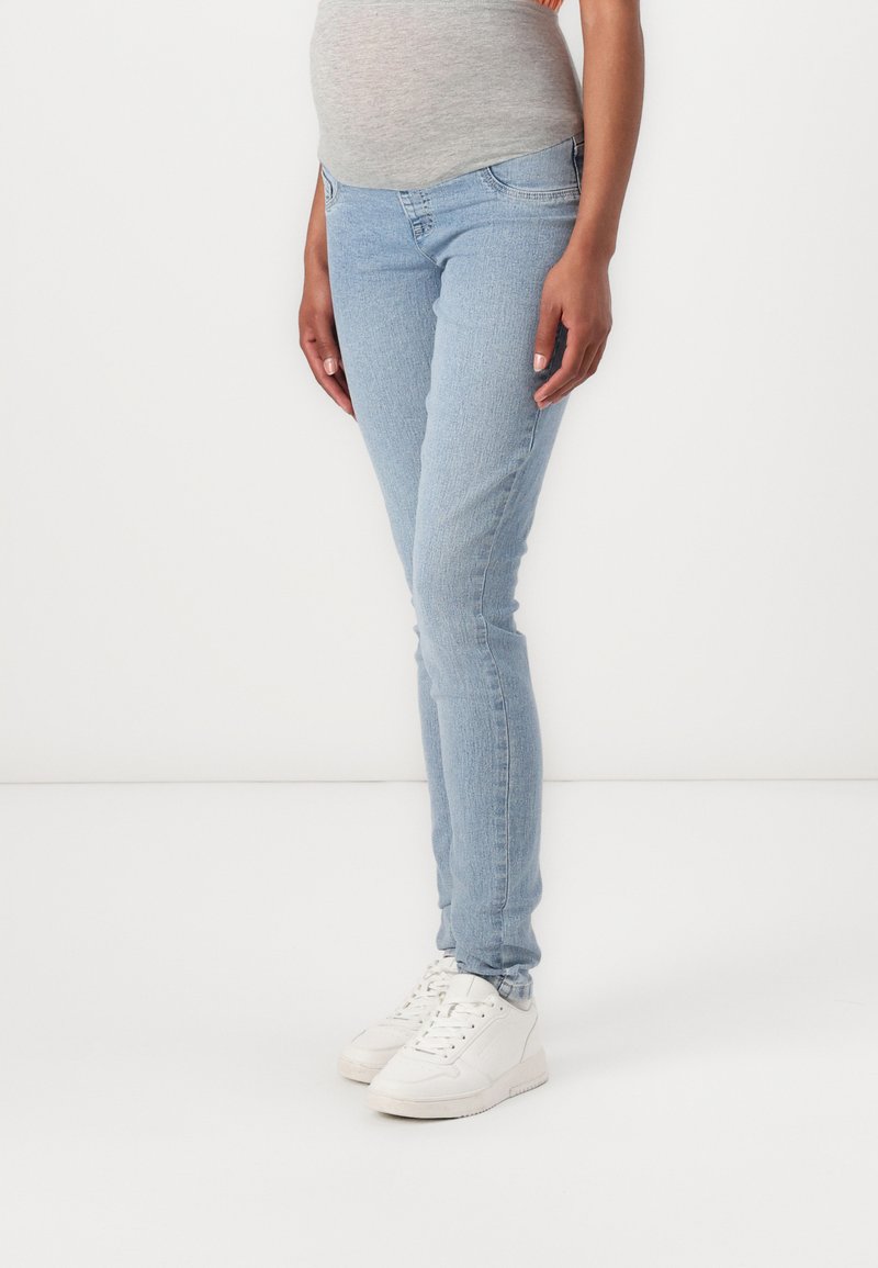 Vaqueros skinnies de denim azul claro con un diseño estándar de cinco bolsillos, ajuste de cintura media y un ligero desgaste en los muslos. Combinados con zapatillas blancas.