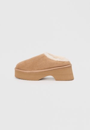 Sabots en suède beige avec une doublure en fausse fourrure, bout rond et une semelle plateforme en bois épaisse. Texture douce et design élévé pour un confort optimal.