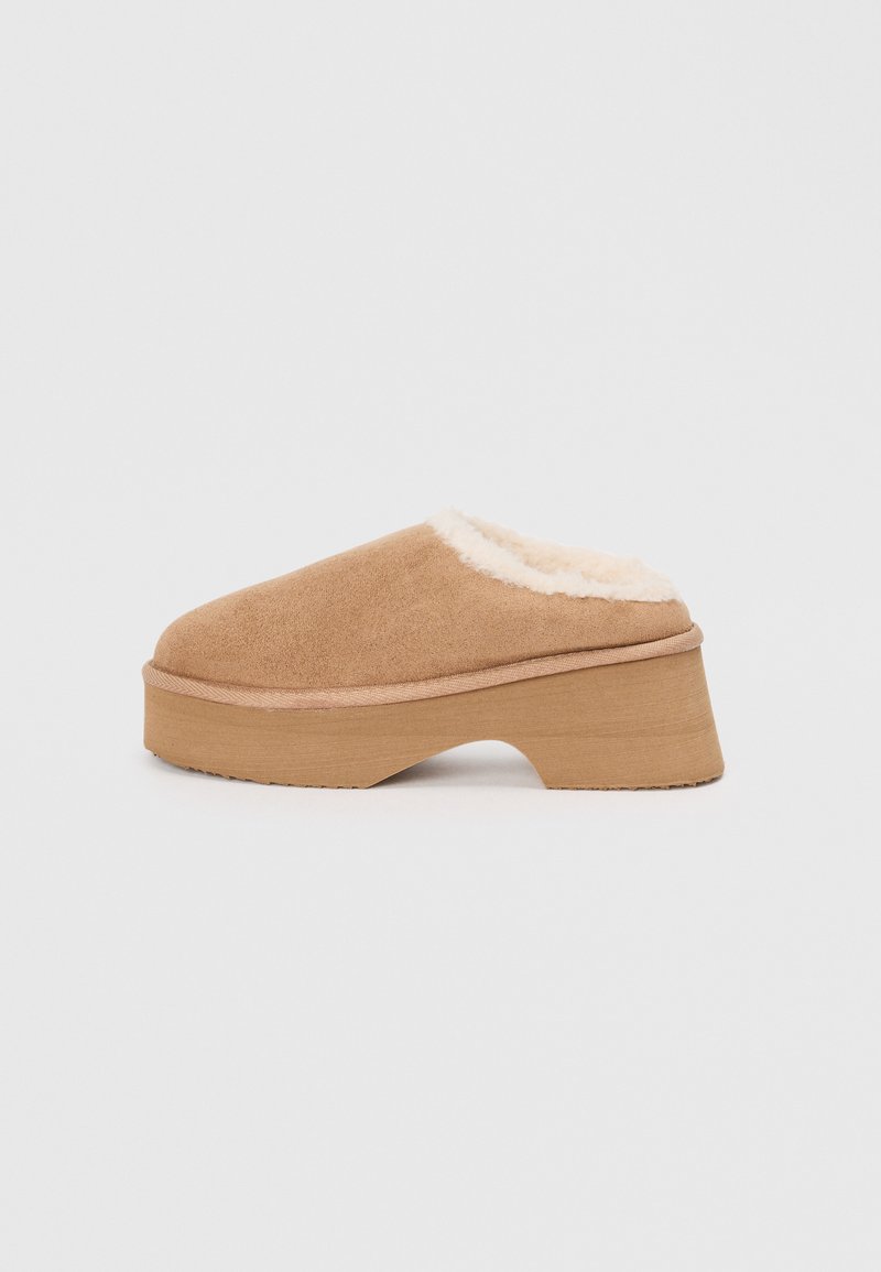 Tan suede clog with a faux fur lining, round toe, and a chunky wooden platform sole. Soft texture and elevated design for comfort.