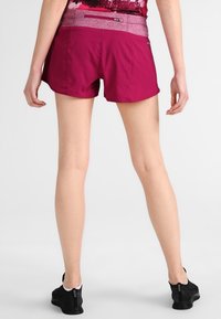 Pantalones cortos deportivos en fucsia con una cintura texturizada. La tela parece ligera y el ajuste está diseñado para facilitar el movimiento.