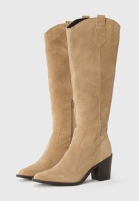 Bottes en suede beige jusqu'au genou avec un bout pointu, une forme effilée, une fermeture éclair verticale et un talon empilé. Présente des accents cousus en haut.