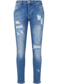 Világoskék skinny farmernadrág, melyen kopott foltok, szakadt szélek és diszkrét fehér festékszórás található. Öt zsebes kialakítású és gombos záródással rendelkezik.