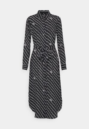 Robe chemise noire à manches longues et devant boutonné. Présente un motif en vagues blanches et un détail de taille nouée. Texture de tissu lisse.