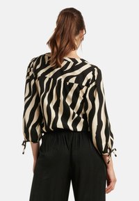 Black and cream zebra-striped blouse with a relaxed fit, three-quarter sleeves, and ties at the sleeves. Soft, smooth fabric texture.