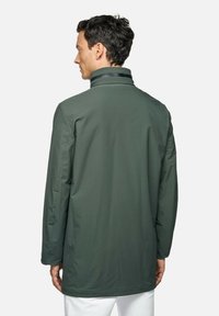 Giacca impermeabile verde con colletto alto, maniche lunghe e una texture liscia, caratterizzata da un taglio di lunghezza media e dettagli di design minimi.