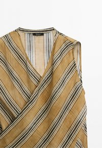 Mouwloze wikkeltop met diagonale beige, zwarte en witte strepen, gemaakt van lichtgewicht gestructureerde stof.