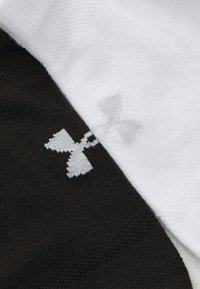 Dos calcetines uno al lado del otro: uno negro con un logo blanco de Under Armour, el otro blanco con un logo gris. Ambos tienen un diseño de punto texturizado.