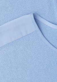 Gros plan d'un pull tricoté bleu clair montrant le col et la zone des épaules avec un détail de tissu lisse.