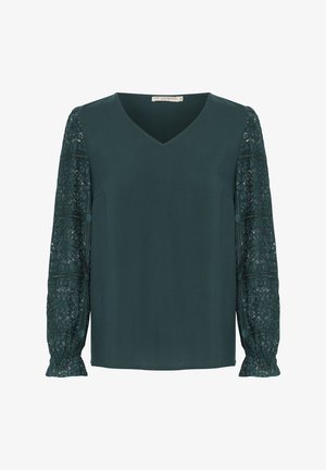 Tumši zaļa blūze ar V-veida kakla izgriezumu, vienkrāsainu priekšpusi un garām mežģīņu piedurknēm ar sarežģītiem rakstiem un savilktiem galiem.