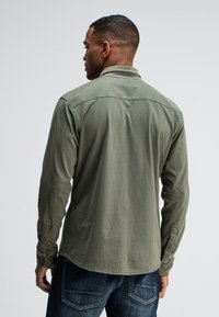 Olivengroen shirt met lange mouwen, knoopmanchetten en een omgeslagen kraag, gemaakt van zachte stof. Heeft een gladde textuur en een afgeronde zoom.