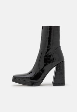 Bottine noire avec un motif crocodile glossy, bout carré et talon épais. Présente une texture lisse et un design élégant.