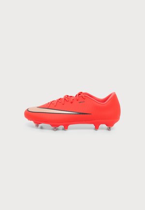 Felrode voetbalschoen met zwarte en beige Nike-swoosh, vetersluiting en zes noppen onder de zool voor grip op een witte achtergrond.
