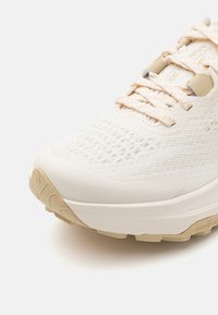 Witte sportschoen met een gestructureerde mesh bovenkant, crème accenten, platte veters en een gevoerde zool met een patroon voor grip.