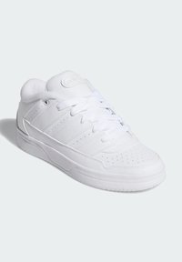 Vit sportskor med en texturerad läderöverdela, perforeringar för ventilation, platta vita snören och en gummiyttersula.