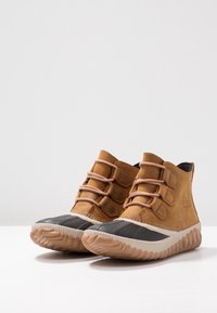 Bottes courtes en cuir marron avec bouts en caoutchouc noir, lacets beige, surface texturée et semelle en caoutchouc naturel striée.