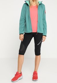 Turkos zip-up jacka med en rosa innerfoder, kombinerad med en rosa T-shirt och svarta capri-leggings. Har röda träningsskor.