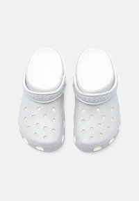 Szare, błyszczące klapki z pianki z wieloma otworami wentylacyjnymi, zaokrąglonym noskiem oraz regulowanym paskiem na pięcie dla zapewnienia stabilnego dopasowania.