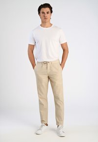 Witte T-shirt met korte mouwen, gecombineerd met lichtbeige broeken met trekkoorden in de taille en witte sneakers. Licht materiaal, relaxte pasvorm, minimalistisch ontwerp.