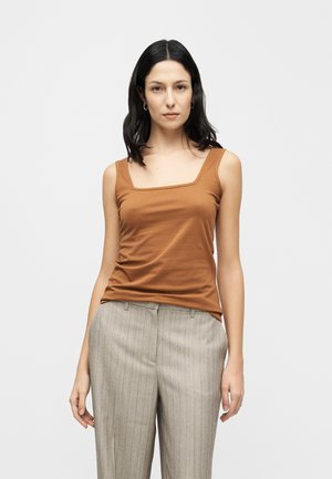 Brun tætsiddende tanktop med firkantet halsudskæring og tynde stropper, parret med lysegrå bukser med nålestriber, på en neutral baggrund.