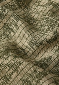 Textil med vågiga gröna mönster på en beige bakgrund, med en texturerad yta och fina linjer som skapar en lager-effekt.