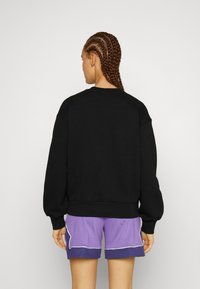 Schwarzer Sweatshirt mit Rundhalsausschnitt und lockerer Passform. Gerippte Bündchen und Saum, über lila Shorts mit weißen Akzenten getragen.