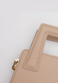 Beżowa torebka z ekoskóry o usztywnionej budowie, z kwadratowym uchwytem i widocznymi detalami szwów. Posiada złote akcenty metalowe.